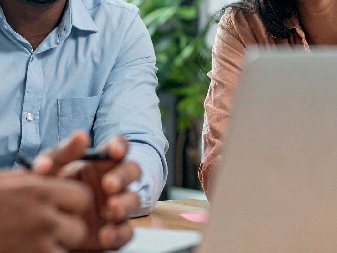 Professional meeting showing three people around a table. Faces are cut off.