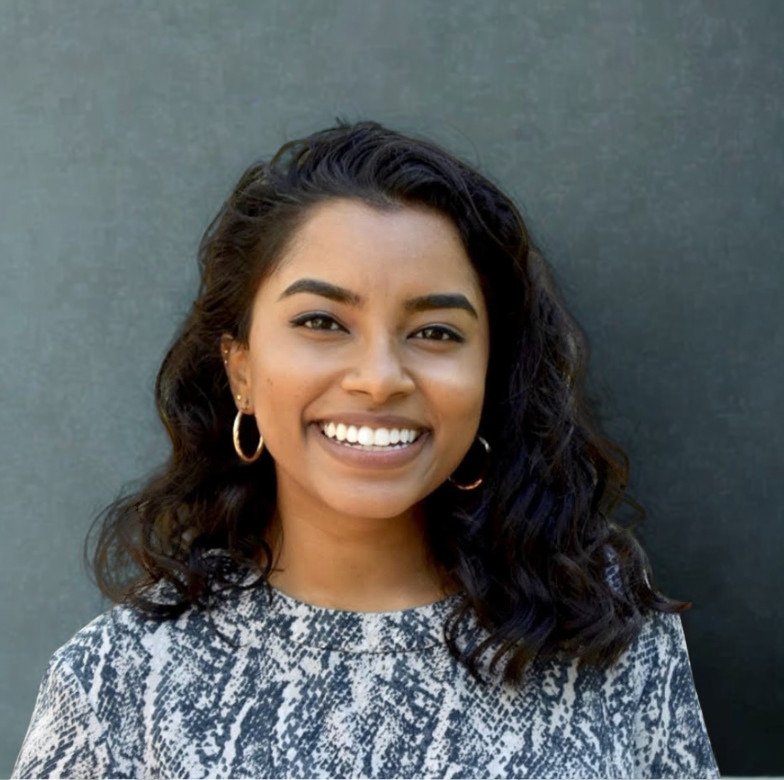 Woman with curly hair smiling at camera, in front of a grey background.